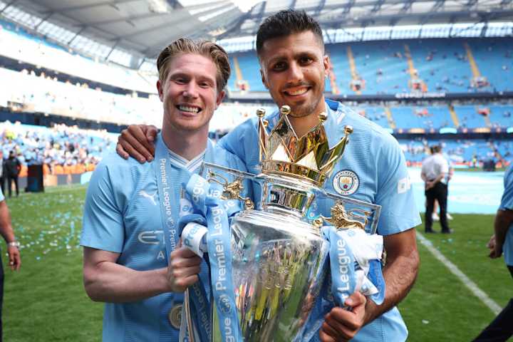 Rodri holding the Premier League title with teammate Kevin De Bruyne